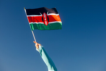 Hand Waiving a Kenyan Flag on a Blue Sky. Cheerful enthusiastic patriotic person displaying the...