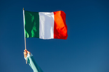 Hand Waiving an Italian Flag on a Blue Sky. Cheerful enthusiastic patriotic person displaying the symbol of Italy

