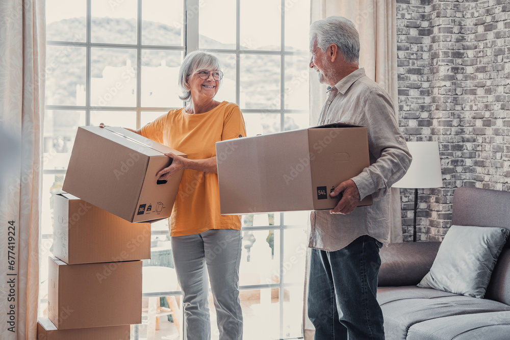 Wall mural mature couple moving into new apartment, carrying cardboard boxes into empty room with potted plants