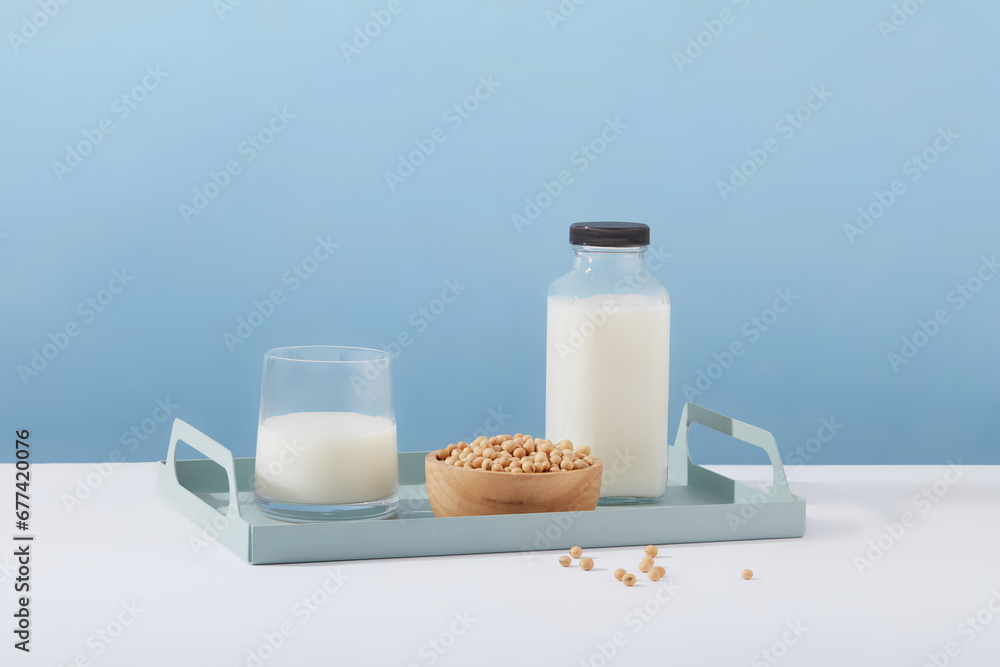 Wall mural Empty label milk bottle arranged on a tray in pastel color with a cup of milk and wooden bowl of soybeans. Template for mockup your design