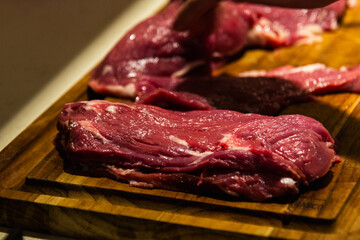 a photograph with raw meat cut into steaks to make cordovan tenderloins with a knife and a close-up of a hand cleaning or tenderizing the meat