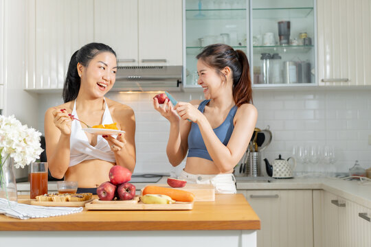 Two healthy Asian female friends in exercise clothes Is happily cooking a healthy meal in her home kitchen in the morning. Healthy care concept, healthy fruit juice, Healthy fruits every day.