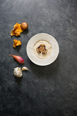 Obraz na płótnie Canvas Cream of wild mushroom soup in a bowl on black background with ingredients around