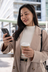 A beautiful Asian businesswoman is responding to messages on her phone while she is in the city.