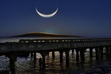 Surreal upside down crescent moon over Lanai at Mala Pier on Maui.
