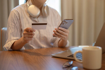 Cropped image of a woman holding a credit card and her smartphone at a table indoors.