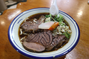 Closed up of Taiwanese style stewed beef noodle with brown soup serving on the timber table
