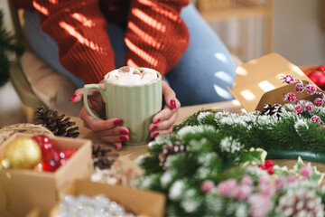 Closeup female hands holding cup of hot cocoa with marshmallow topping.