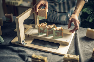 Women's hands cut homemade natural soap on a professional wood cutter. A means of eco-friendly hygiene