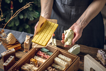 A soap maker woman holds a piece of cocoa butter and a bar of cosmetic chocolate in her hands. A lot of different sliced pieces. Eco-friendly natural handmade cosmetics