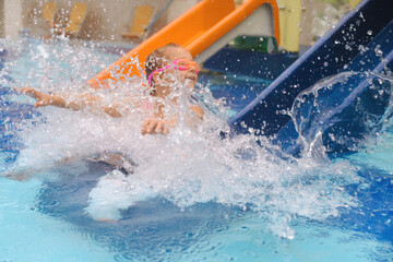 Child sliding into the water in aqua park. Kid having fun and entertaining in indoor swimming pool....