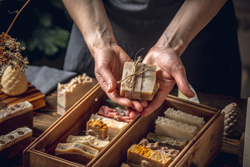A woman soap maker holds handmade soap in her hands. A lot of different sliced pieces in a wooden...