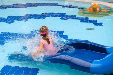Child sliding into the water in aqua park. Kid having fun and entertaining in indoor swimming pool....