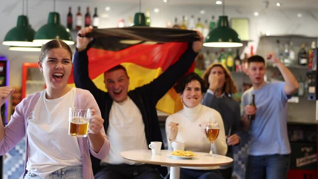 Smiling man and woman with Germany flag drinking alcohol and having conversation on party in nightclub