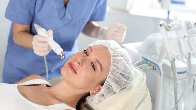 Young woman cosmetologist doing microcurrent procedure to young woman. High quality 4k footage