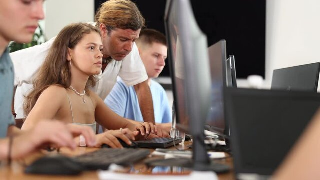 Motivated young female trainee working at IT startup sitting at computer while male mentor explaining assigned task and giving advices on solution