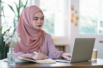 Millennial Asian Muslim freelancer businesswoman working remotely online using a laptop at a cafe.