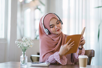 An Asian Muslim university student relaxes while reading a book at home.