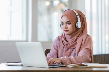 Asian Muslim university student studying remotely, using laptop and listening to online lecture.