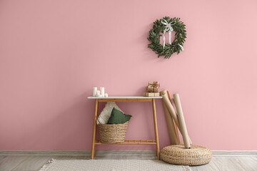 Table with candles, gifts and Christmas wreath hanging on pink wall in room. Banner for design