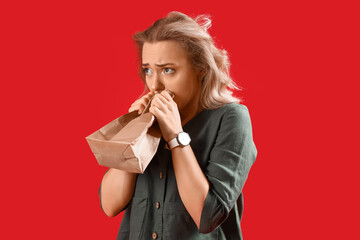 Young woman with paper bag having panic attack on red background