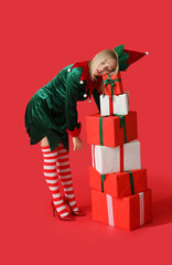Young woman in elf costume with Christmas gift boxes on red background