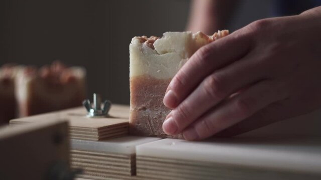 A female master soap maker cuts bright natural handmade soap on a wooden string cutter. Home production of natural cosmetics