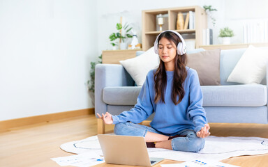 Happy young Asian woman practicing yoga and meditation at home sitting on floor in living room in...