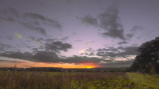 Aerial drone hyperlapse of a sunset in a rural countryside that shows vast fields, grasslands, and some trees.