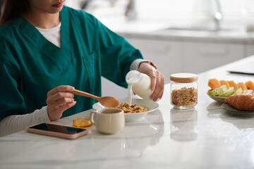 Cropped image of woman pouring milk in bowl with cornflakes and muesli
