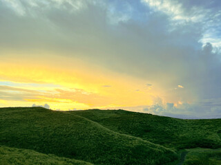 the nature mountain ridge landscape yellow sunrise or sunset view is a green grass meadow and highland hill mountain with white cloud cloudy cloudscape on a blue beautiful bright sunlight sky
