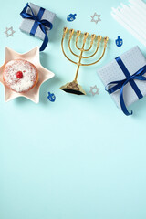 Hanukkah concept with this festive flat lay featuring menorah, candles, sufganiyot, and gift boxes on pastel blue background.