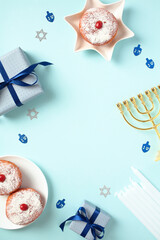 Hanukkah flat lay composition with golden menorah, sufganiyot, candles, and gift boxes set on pastel blue backdrop. Jewish symbols, perfect for creating cheerful greeting cards or banners."
