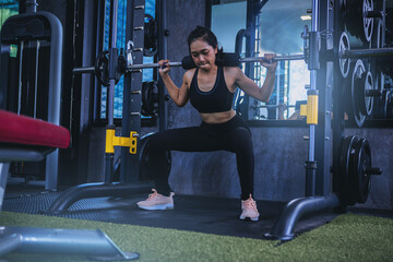 Fit young woman holding her hands with a weight barbell for pulling, squatting, workout in the fitness gym.