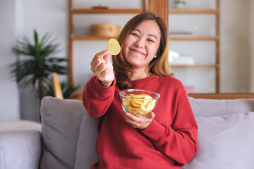 Portrait image of a young woman picking and eating potato chips at home - obrazy, fototapety, plakaty