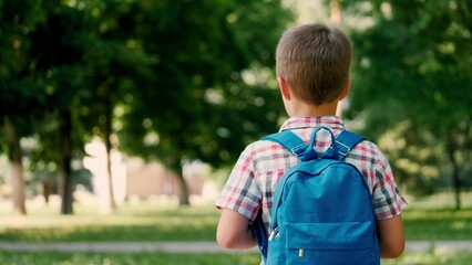 Junior schoolboy dressed in checkered shirt walks to school through city park