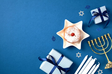 Hanukkah celebration flat lay with golden menorah, candles, sufganiyot, and gift boxes. Happy Chanukah greeting card with Jewish decor on blue background. - obrazy, fototapety, plakaty