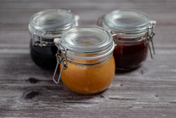 Assortment of homemade jams. Jams in glass jars, oranges, strawberries and blueberries. Front view of seasonal fruits in jam or marmalade.