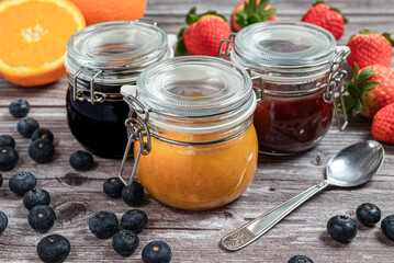 Assortment of homemade jams. Jams in glass jars, oranges, strawberries and blueberries. Front view,...