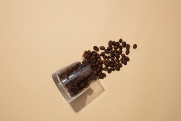 Top view of a glass cup containing coffee beans and pouring out on a beige background. Take photos to advertise natural ingredients, often used in beauty cosmetics with many uses