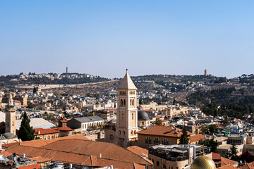 Fototapeta na wymiar Panoramic view on old part of Jerusalem city, Israel. Ancient jewish city shot from above on a sunny cloudless day. Tiled roofs, chapels and dome of churches of Jerusalem at blue sky background.