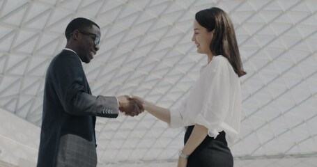 Man and woman colleagues talking shaking hands and leaving innovative office building. Ambitious businesspeople and successful partnership concept.