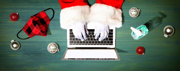Santa Claus using a laptop computer with a mask and a sanitizer bottle from above - obrazy, fototapety, plakaty