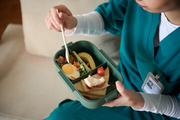 Medical nurse with lunchbox eating salad and sandwiches in hospital lounge area
