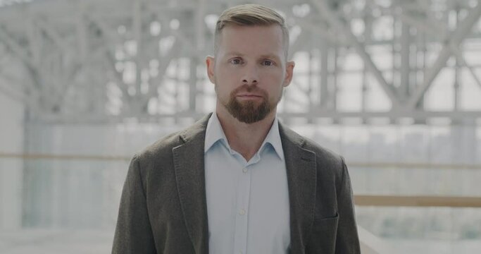 Slow motion portrait of elegant employee standing in modern glass wall business center at work and looking at camera. Businessperson and successful career concept.