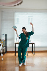 Medical nurse in green scrubs dancing in hospital lounge area after finishing shift - obrazy, fototapety, plakaty