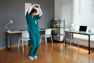 Happy young woman in scrubs dancing after finishing internship in hospital