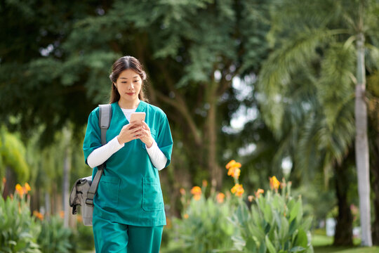 Young Vietnamese medical nurse checking notifications on smartphone when walking to hospital