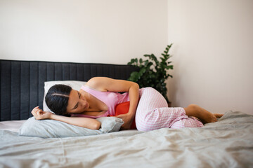 Woman at home suffering from menstrual pain. Menstrual cramps, woman warming lower abdomen with a...