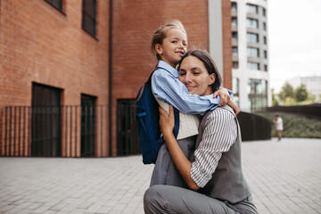 Working mother hugging daughter in front of the school building, and heading to work. Concept of...